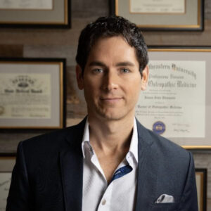 Dr. Jason Pirozzolo, DO, in front of his framed medical diplomas